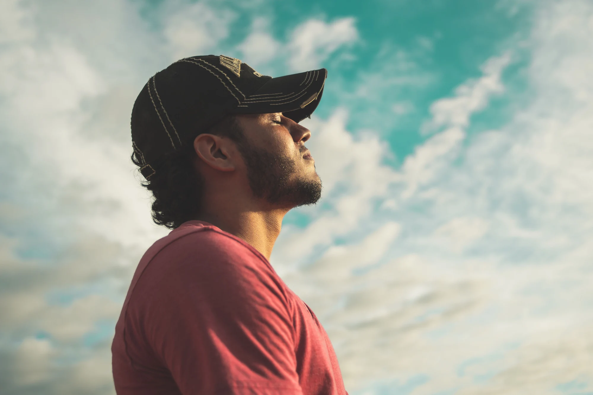 A relaxed man with his eyes closed, enjoying warm sunshine on his face beneath an open sky